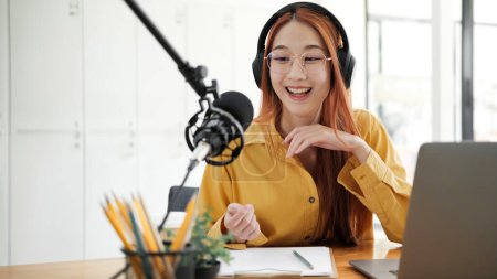 Photo for Cheerful woman hosting a live podcast, engaging with audience using professional microphone in studio. - Royalty Free Image