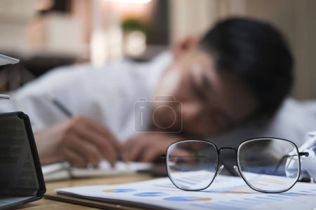 Foto de Exhausto hombre de negocios durmiendo en su escritorio de la oficina, al lado de la computadora portátil y documentos, cansado de exceso de trabajo. - Imagen libre de derechos