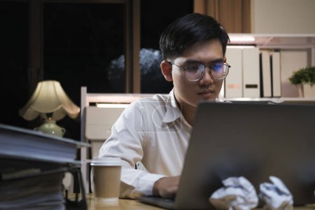 Photo for Young Asian businessman working tired office worker sitting at desk using computer and doing overtime project. - Royalty Free Image