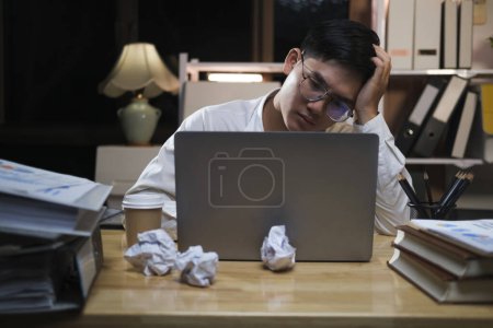 Photo for Asian young tired staff businessman using desktop computer having overwork project overnight in office, exhausted unhappy businessman feeling sleepy after after working hard overtime at night. - Royalty Free Image