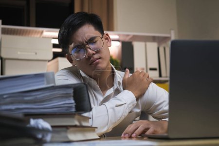 Foto de Asiático hombre de negocios horas extras de trabajo y sentir dolor de hombro en la oficina sensación de cansancio, fatiga, agotado mientras se trabaja horas extras en la noche en la oficina. - Imagen libre de derechos