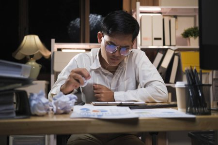 Téléchargez les photos : Asiatique travaillant tard assis sur le bureau dans les heures supplémentaires de bureau la nuit. Homme d'affaires se sentant fatigué et le stress pour un travail surchargé. - en image libre de droit