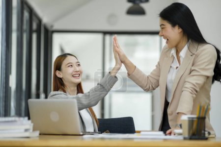 Foto de Dos mujeres de negocios alegres dando un máximo de cinco en un entorno de oficina, celebrando una exitosa colaboración.. - Imagen libre de derechos