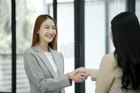 Téléchargez les photos : Deux femmes d'affaires souriantes serrant la main d'un bureau dans le bureau, symbolisant un accord ou un partenariat réussi. - en image libre de droit