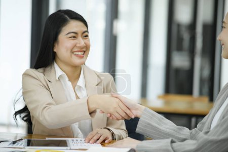 Photo for Two smiling businesswomen shaking hands over a desk in the office, symbolizing a successful agreement or partnership. - Royalty Free Image