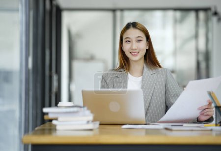 Foto de Una empresaria profesional y confiada sonriendo a la cámara, de pie junto a su escritorio con un portátil en una oficina moderna. - Imagen libre de derechos