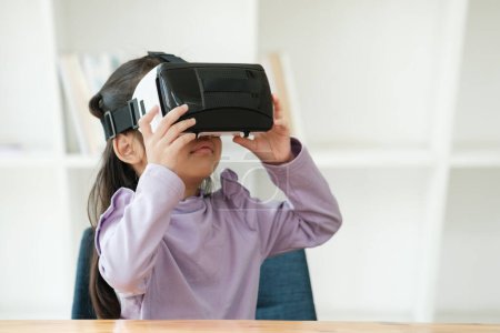 Foto de Una niña de edad elemental utiliza un auricular de realidad virtual para mejorar la experiencia de aprendizaje con emoción. Marketing para productos VR, contenido de tecnología educativa. - Imagen libre de derechos