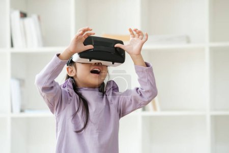 Téléchargez les photos : Une fillette du primaire utilise un casque de réalité virtuelle pour améliorer l'expérience d'apprentissage avec excitation. Marketing pour les produits VR, contenu technologique éducatif. - en image libre de droit