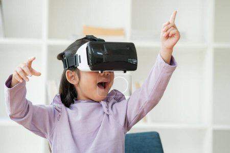 Foto de Una niña de edad elemental utiliza un auricular de realidad virtual para mejorar la experiencia de aprendizaje con emoción. Marketing para productos VR, contenido de tecnología educativa. - Imagen libre de derechos