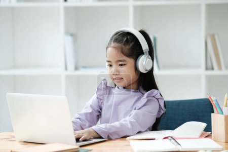 Photo for A young girl is sitting at a desk with a laptop and headphones on. She is smiling and she is enjoying her work. The scene suggests that she is engaged in an educational or creative activity - Royalty Free Image