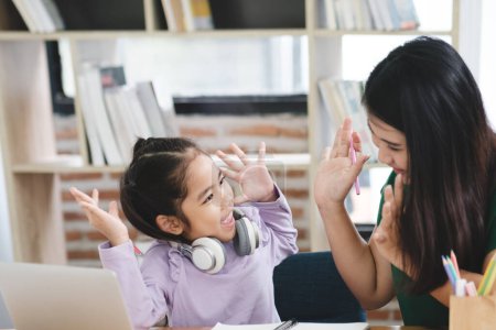 Photo for A young girl is playing with a laptop while her mother watches. The girl is wearing headphones and he is enjoying herself. Concept of warmth and happiness - Royalty Free Image
