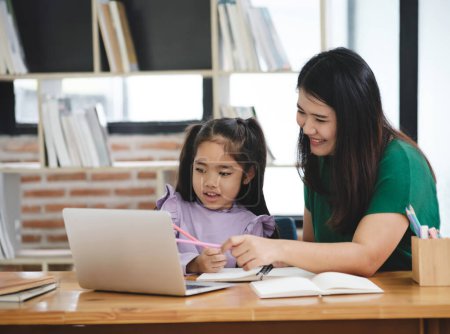 Photo for A woman is helping a young girl with her homework. The girl is using a laptop and a pencil. The woman is smiling and she is patient and supportive. The scene suggests a positive - Royalty Free Image