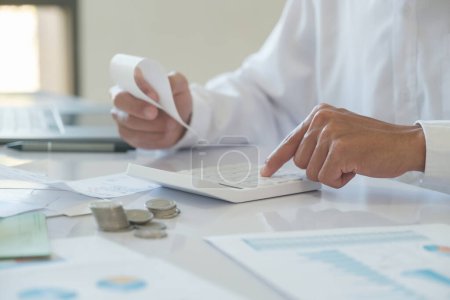 Photo for An accountant in is using a calculator to calculate bill income and investment information to manage the financial budget used for investment - Royalty Free Image