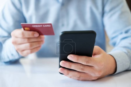 Téléchargez les photos : Un homme utilise son téléphone pour payer une carte de crédit. Il tient la carte de crédit dans une main et le téléphone dans l'autre - en image libre de droit