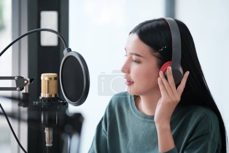 Photo for A woman is recording a song in a studio. She is wearing headphones and smiling. The studio is equipped with a microphone and a soundboard. The woman is enjoying the recording process - Royalty Free Image