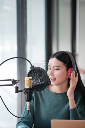 Photo for A woman is recording a song in a studio. She is wearing headphones and is smiling. The studio is equipped with a microphone and a laptop - Royalty Free Image