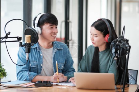 Photo for Two people are sitting at a desk with a laptop and a microphone. They are smiling and seem to be enjoying each others company - Royalty Free Image