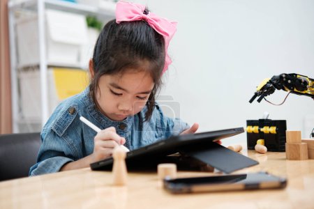 Téléchargez les photos : Jeune fille concentrée en denim à l'aide d'un stylet pour dessiner sur une tablette numérique, embrassant la technologie dans l'éducation. - en image libre de droit