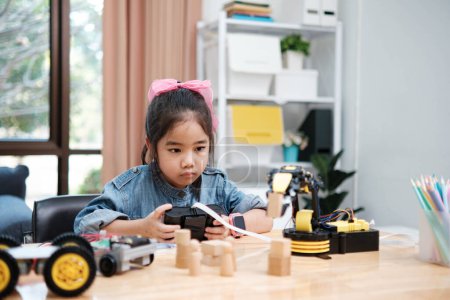 Photo for A primary school girl focuses on operating a robotic arm with a remote control, demonstrating STEM education in action. - Royalty Free Image