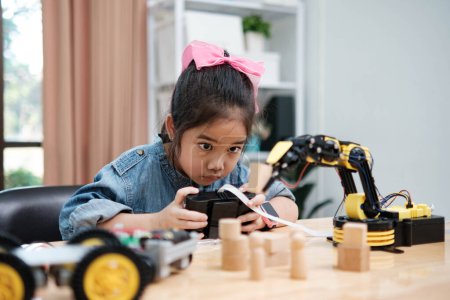 Foto de Una niña de primaria se centra en operar un brazo robótico con un control remoto, lo que demuestra la educación STEM en acción. - Imagen libre de derechos