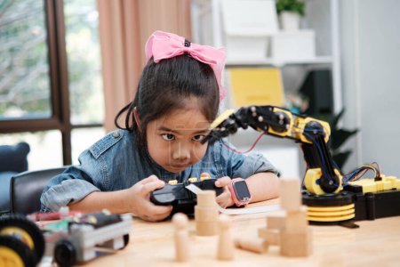 Téléchargez les photos : Une écolière du primaire se concentre sur l'utilisation d'un bras robotisé avec télécommande, démontrant l'éducation aux STIM en action. - en image libre de droit