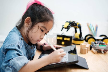 Photo for A primary school girl focuses on operating a robotic arm with a remote control, demonstrating STEM education in action. - Royalty Free Image