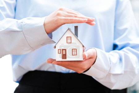 Téléchargez les photos : Gros plan sur les mains berçant un modèle de maison, symbolisant la protection et les soins dans les secteurs de l'assurance immobilière et immobilière - en image libre de droit