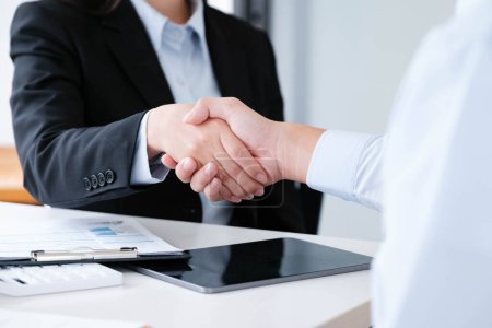 Photo for Close-up of a professional handshake between colleagues sealing a business deal, with work documents and tablet in background. - Royalty Free Image