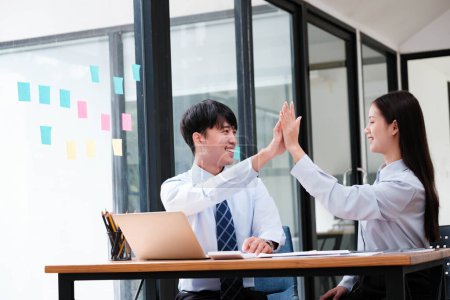 Photo for Two elated business colleagues giving a high-five over a successful project at their office workspace. - Royalty Free Image