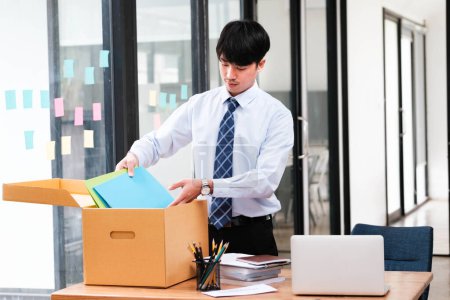 Téléchargez les photos : Un homme en costume ouvre une boîte en carton sur un bureau. La boîte contient des papiers et un ordinateur portable - en image libre de droit