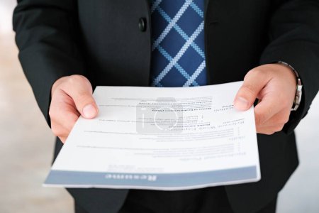 Close-up of a businessmans hands carefully examining a resume, focusing on qualifications for a job candidate.