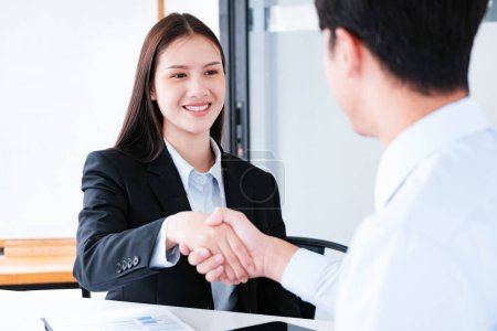 A young businesswoman smiles while shaking hands, making a positive impression during a professional meeting.