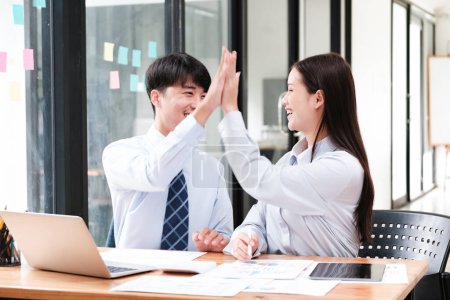 Photo for Two elated business colleagues giving a high-five over a successful project at their office workspace. - Royalty Free Image