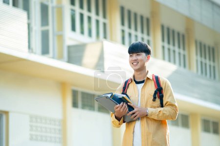 Foto de Un estudiante universitario satisfecho llevando una computadora portátil y libros camina por los terrenos del campus, exudando una sensación de preparación y entusiasmo por el aprendizaje. - Imagen libre de derechos