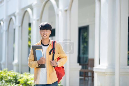Photo for A contented college student carrying a laptop and books walks across the campus grounds, exuding a sense of readiness and enthusiasm for learning. - Royalty Free Image