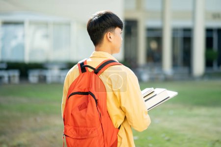 Photo for A university student stands thoughtfully on campus, gazing into the distance with his books in hand, ready for a day of studies. - Royalty Free Image