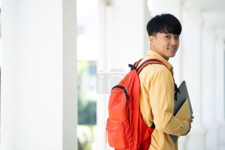 Téléchargez les photos : Un étudiant se tient dans le couloir de son école, tenant des manuels scolaires et souriant, prêt pour une journée d'apprentissage et d'études. - en image libre de droit