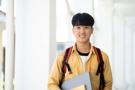 Foto de Un estudiante universitario se para en el pasillo de su escuela, sosteniendo libros de texto y sonriendo, listo para un día de aprendizaje y estudios. - Imagen libre de derechos