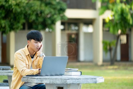Photo for A university student is absorbed in thought while studying on his laptop, sitting at an outdoor table surrounded by the tranquility of the campus. - Royalty Free Image