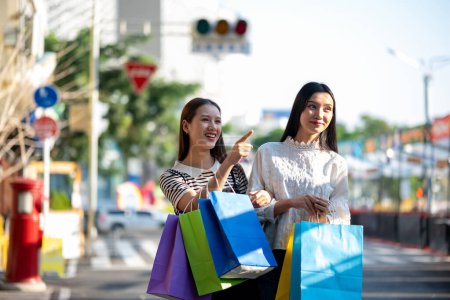 Foto de Se ve a dos mujeres jóvenes disfrutando de un día de compras en la ciudad, sosteniendo coloridas bolsas de compras y compartiendo sonrisas. - Imagen libre de derechos