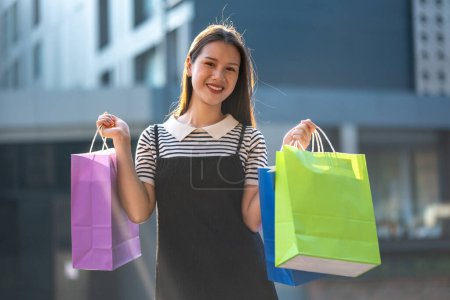 Joyeux jeune femme profitant d'une virée shopping, tenant des sacs à provisions colorés dans un cadre extérieur ensoleillé.