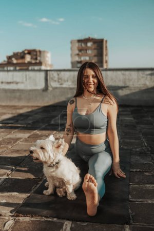 Téléchargez les photos : Relaxed woman practicing yoga stretching exercise on a rooftop supporting by her pet dog. - en image libre de droit