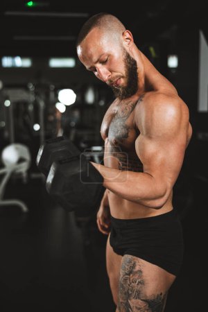 Téléchargez les photos : Prise de vue d'un bodybuilder musclé faisant l'entraînement dur avec haltère à la salle de gym. Il pompe son muscle biceps avec un poids lourd. - en image libre de droit