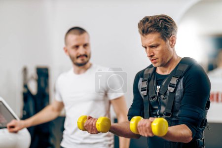 Téléchargez les photos : Homme d'âge moyen fait de l'entraînement EMS avec l'entraîneur dans la salle de gym. - en image libre de droit