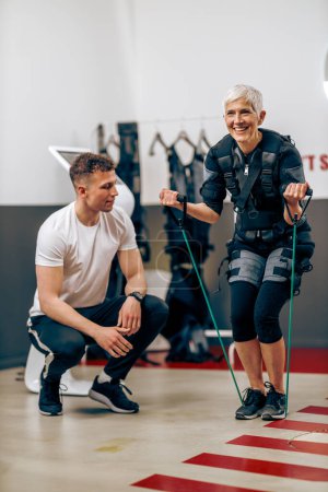 Foto de Senior woman is doing EMS training with personal trainer in the gym. - Imagen libre de derechos