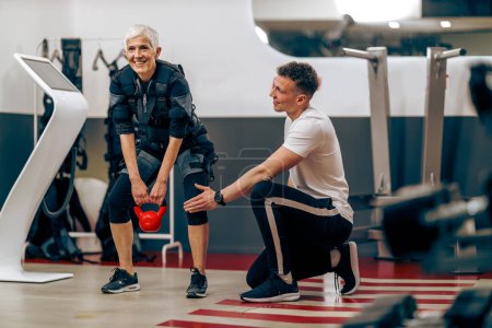 Foto de Senior woman is doing EMS training with personal trainer in the gym. - Imagen libre de derechos