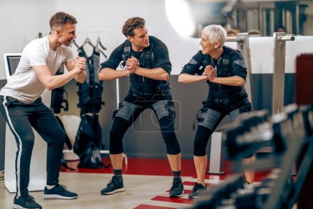 Foto de A senior mother and her middle age son have a EMS workout with personal trainer in the gym. - Imagen libre de derechos
