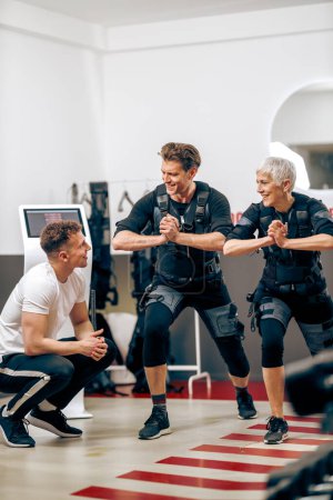 Foto de A senior mother and her middle age son have a EMS workout with personal trainer in the gym. - Imagen libre de derechos