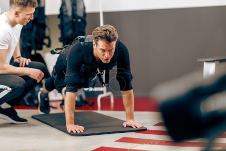 Foto de Middle age man is doing plank exercise during EMS training with coach in the gym. - Imagen libre de derechos
