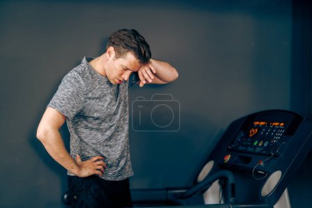Téléchargez les photos : Shot of a tired middle age man is resting after jogging on a treadmill. - en image libre de droit
